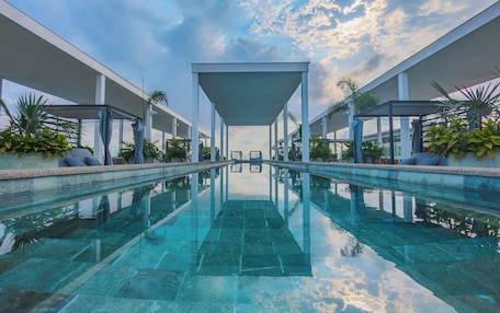 A modern pool area with clear water, white columns, and potted plants.