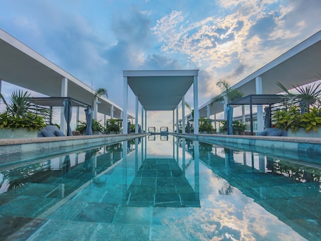 A modern pool area with clear water, surrounded by white columns and covered seating areas.
