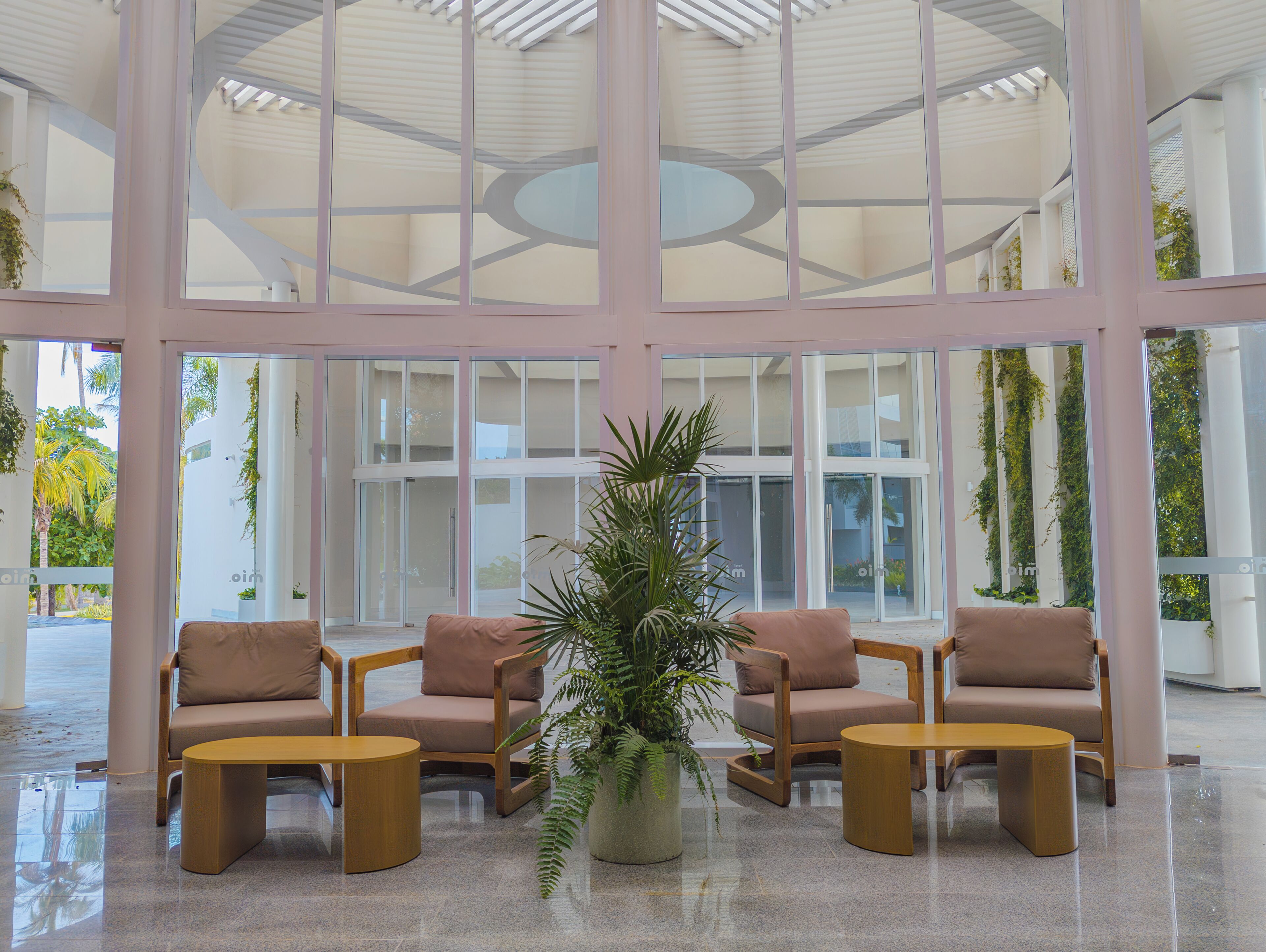Een ruime hal met een modern design, met een zithoek met stoelen en een grote plant in pot.