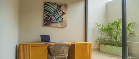 A workspace with a laptop, a chair, and a painting on the wall.
