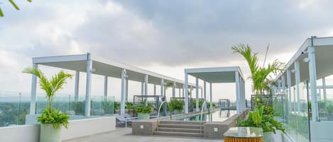 A rooftop terrace with glass railings, outdoor seating, and potted plants.