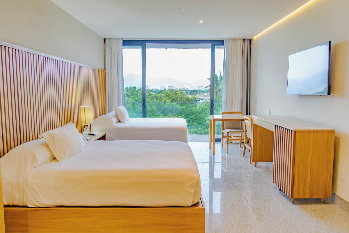 Habitación de hotel con dos camas, un escritorio, una silla, un televisor y un balcón con vistas.