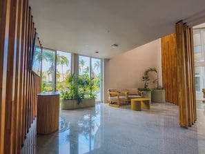 Un lobby moderno con piso pulido, paneles de madera y un área de descanso con dos sillas y una mesita.