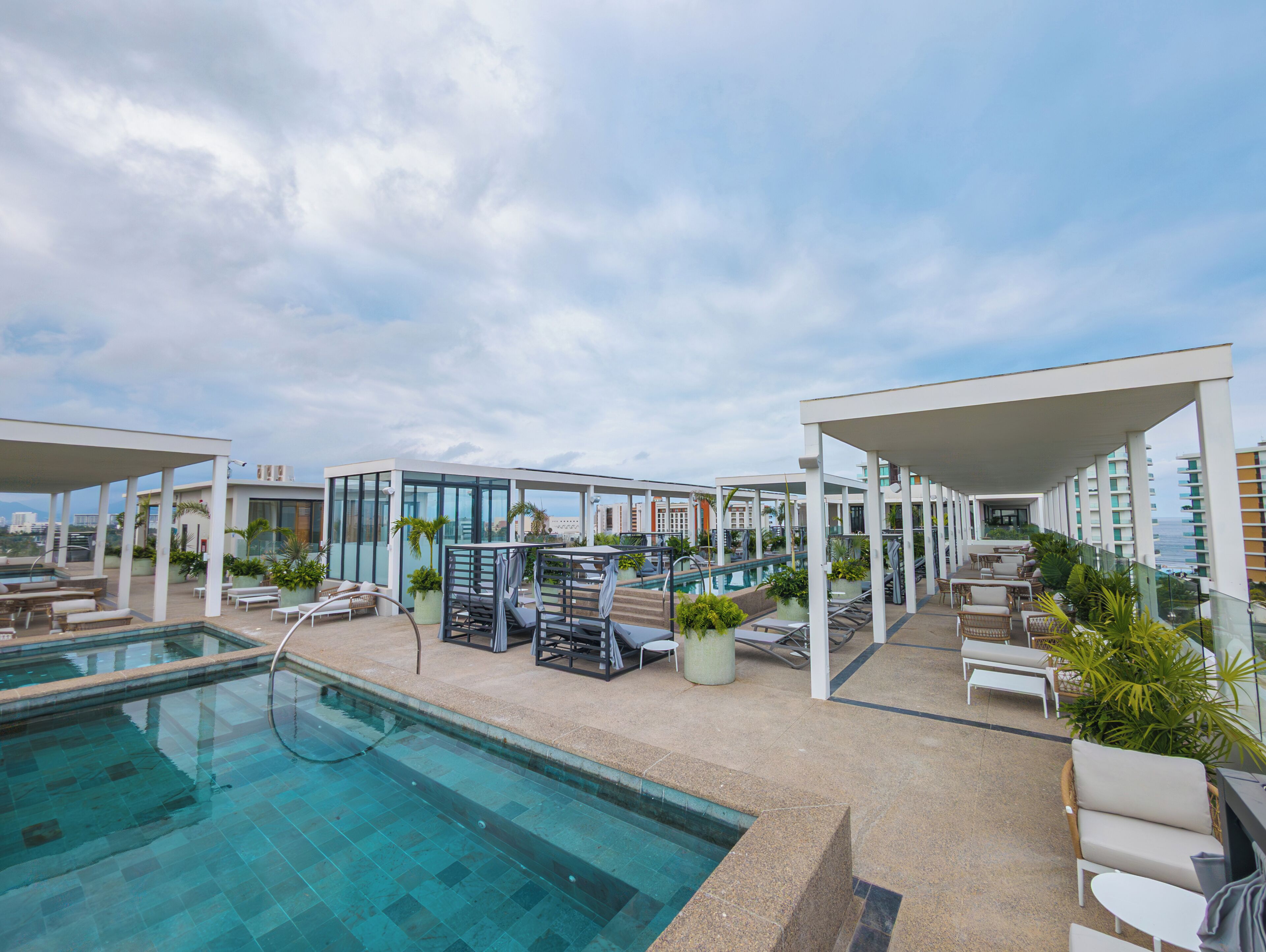 A rooftop pool area with lounge chairs and a glass-enclosed cabana.