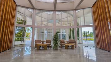 A spacious lobby with a high ceiling, large windows, and a central seating area with chairs and a table.