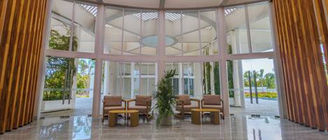 A spacious lobby with a high ceiling, large windows, and a central seating area with chairs and a table.