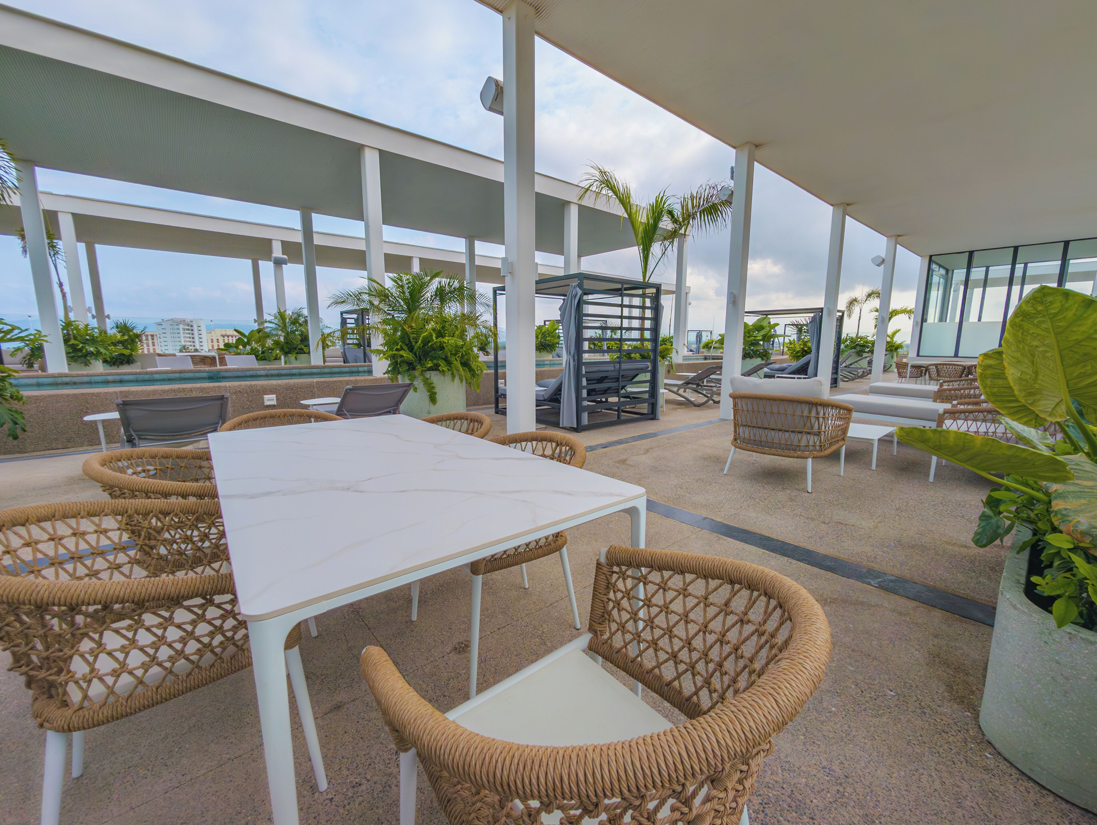 Un patio al aire libre con una mesa blanca, sillas de mimbre y una zona de estar con vista al océano.