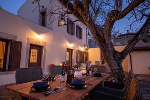 An outdoor dining area with a wooden table set for four, surrounded by wicker chairs, under a tree. - Walnut Tree Villa Ano Archanes-10km From Heraklion (Archanes-Asterousia)