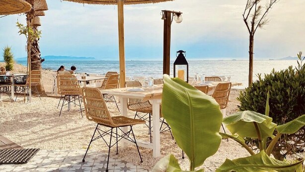 A beachside patio with wicker chairs, a round table, and a large umbrella. - The Black Marble - Sea View / 2BR / 1,5BA (Paleo Faliro)