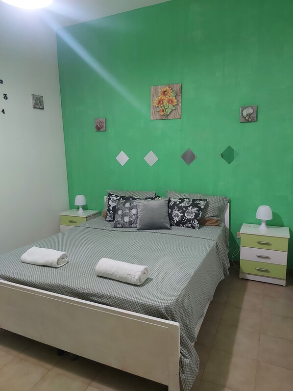 Une chambre à coucher bien rangée, avec un lit, deux tables de chevet et un mur vert.