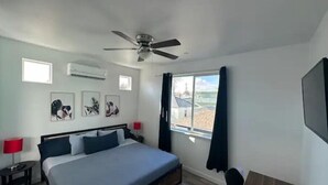 A bedroom with a bed, ceiling fan, artwork, window, and a TV. - One Bedroom Hideaway (Reno)