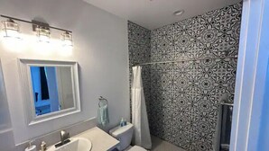 A bathroom with a sink, toilet, and shower. The walls have a patterned tile design. - One Bedroom Hideaway (Reno)