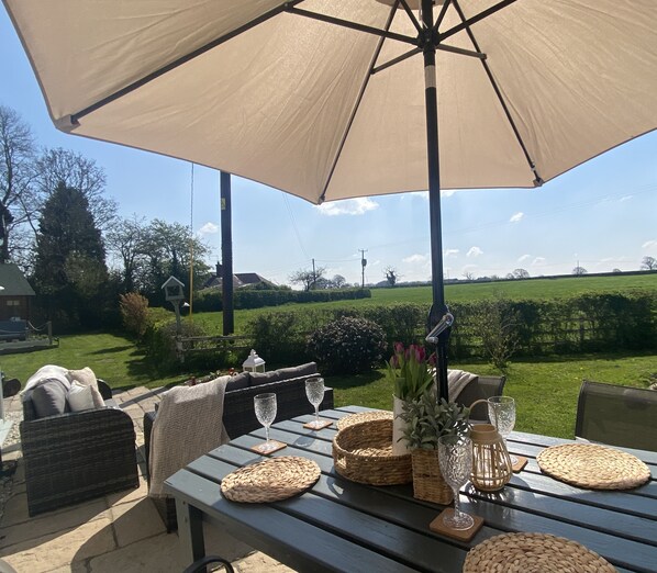 An outdoor patio with a table set for dining, surrounded by wicker furniture and a large umbrella.