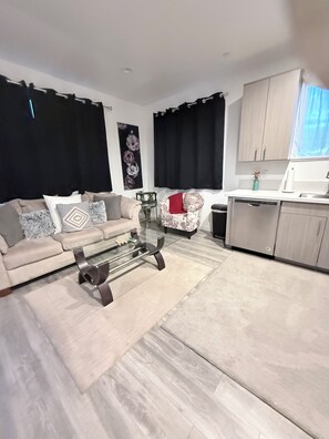 A modern living room with a sofa, coffee table, and a kitchen area with cabinets and a sink.