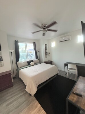 A bedroom with a bed, a desk, a chair, a ceiling fan, and an air conditioning unit.