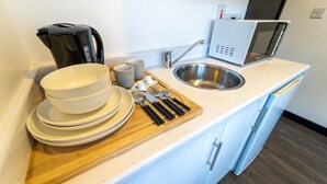 Ett kök med diskho, mikrovågsugn, kaffebryggare och en skärbräda i trä med tillhörande köksredskap.