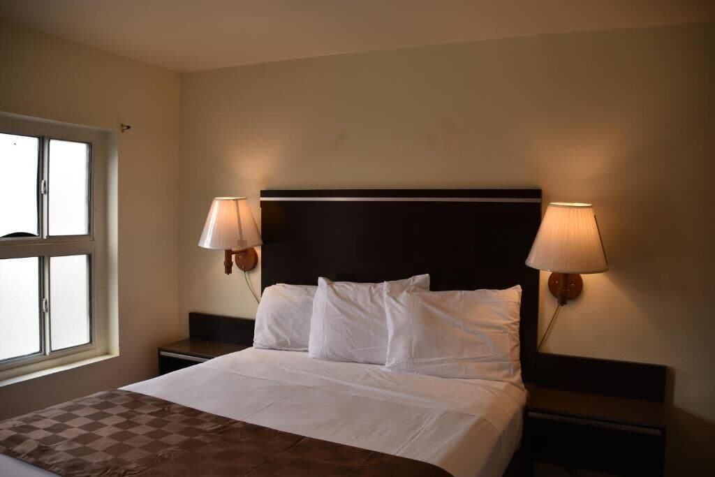 A hotel room with a large bed, two bedside lamps, a window, and a checkered throw blanket.