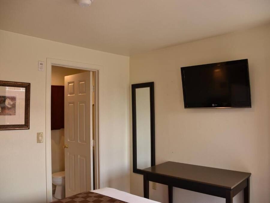 A hotel room with a bed, a television mounted on the wall, a door leading to a bathroom, and a framed picture on the wall.