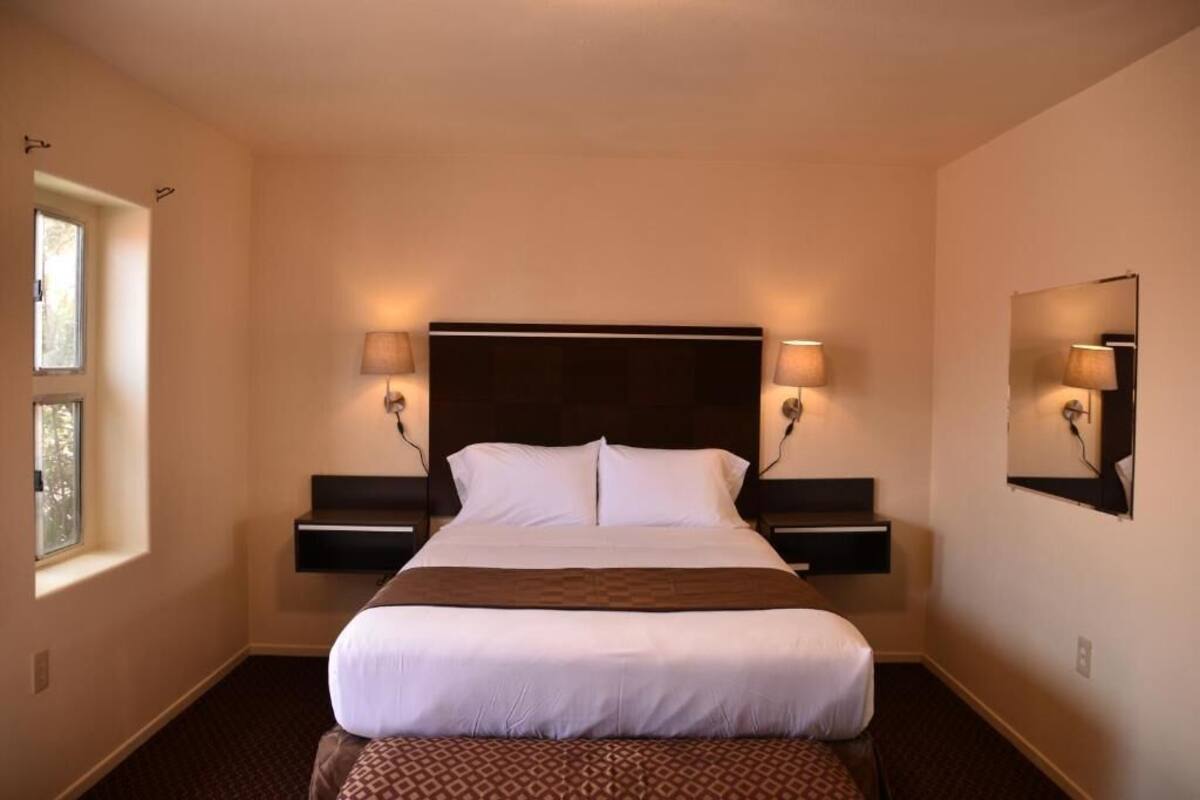A hotel room with a large bed, two bedside tables with lamps, a window, and a wall-mounted mirror.