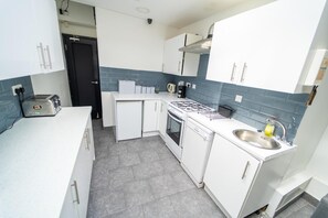 A compact kitchen with white cabinets, a gas stove, a dishwasher, and a sink.
