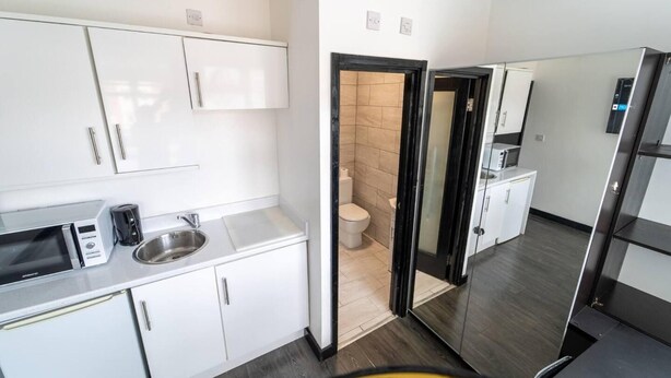A modern kitchen with white cabinets, a stainless steel sink, a microwave, and a refrigerator. - Stunning Studio Next to Restaurants! (Birmingham)