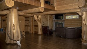 Interieur van een blokhut met houten plafond, een open haard, lederen zitplaatsen en een opgehangen herten schedel.