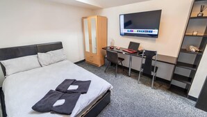 Ein Hotelzimmer mit Bett, Schreibtisch, Stuhl, Fernseher und Kleiderschrank.
