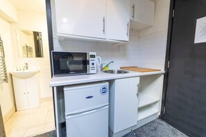 Una kitchenette compacta con microondas, pileta y heladera pequeña.