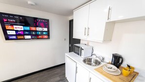 Une cuisine moderne équipée d’un téléviseur à écran plat permettant d’accéder aux services de diffusion en continu, d’un four à micro-ondes, d’un évier et d’une machine à café.