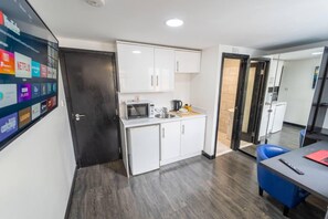 A modern kitchen with white cabinets, a microwave, and a coffee maker. There is a blue chair and a table with a remote control.