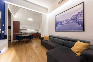 Un salon moderne avec un canapé et une table à manger, un coin cuisine avec des placards et un grand tableau encadré au mur.