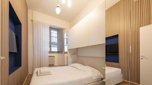 Een moderne slaapkamer met een bed, een ingebouwde televisie en een raam met gordijnen.