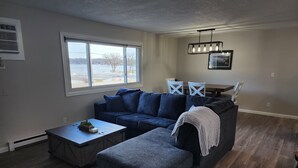 A living room with a sectional sofa, a coffee table, and a dining table with chairs. - Green Lake Condo in the heart of Spicer (Spicer)