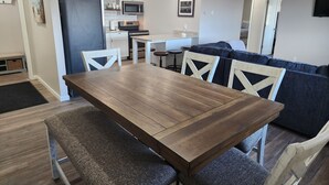 A modern kitchen with white cabinets, a microwave, and a built-in oven. There is a dining area with a wooden table and chairs, and a dark blue sofa in the background. - Green Lake Condo in the heart of Spicer (Spicer)