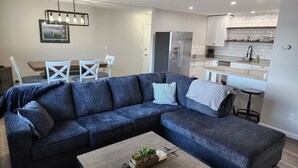 A modern living room with a sectional sofa, a coffee table with plants, and a dining area with a wooden table and white chairs. - Green Lake Condo in the heart of Spicer (Spicer)