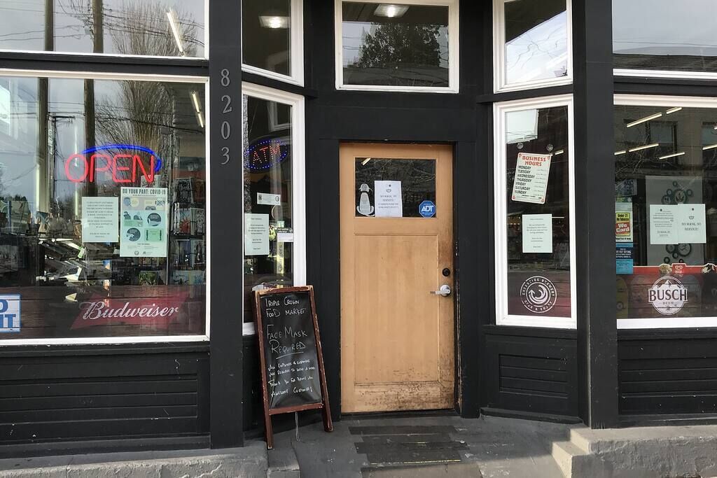 A storefront with a closed wooden door, a sign indicating business hours, and a chalkboard sign stating 'Face Mask Required'.