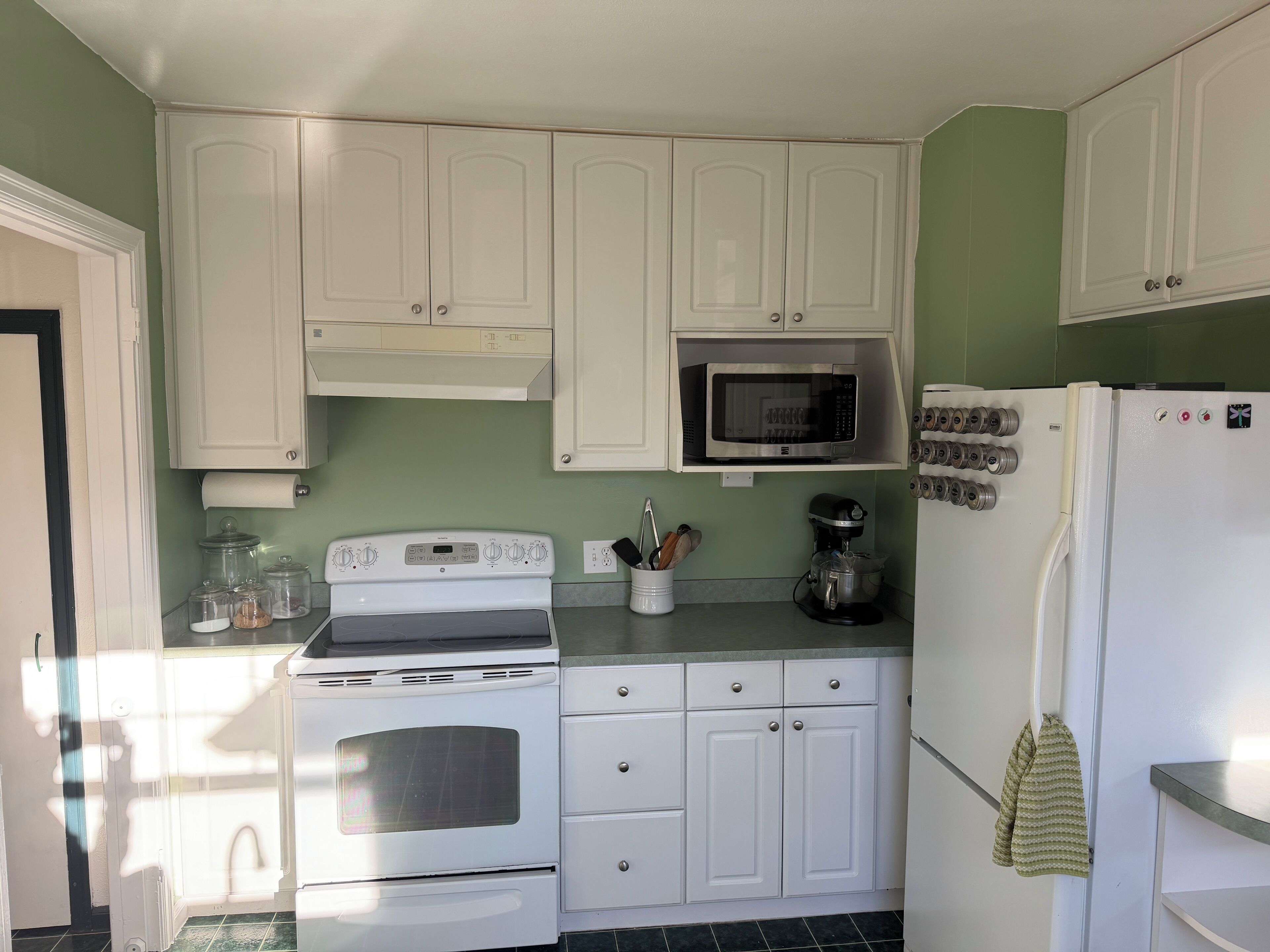 A compact kitchen with white cabinets, a microwave, a stove, and a refrigerator.