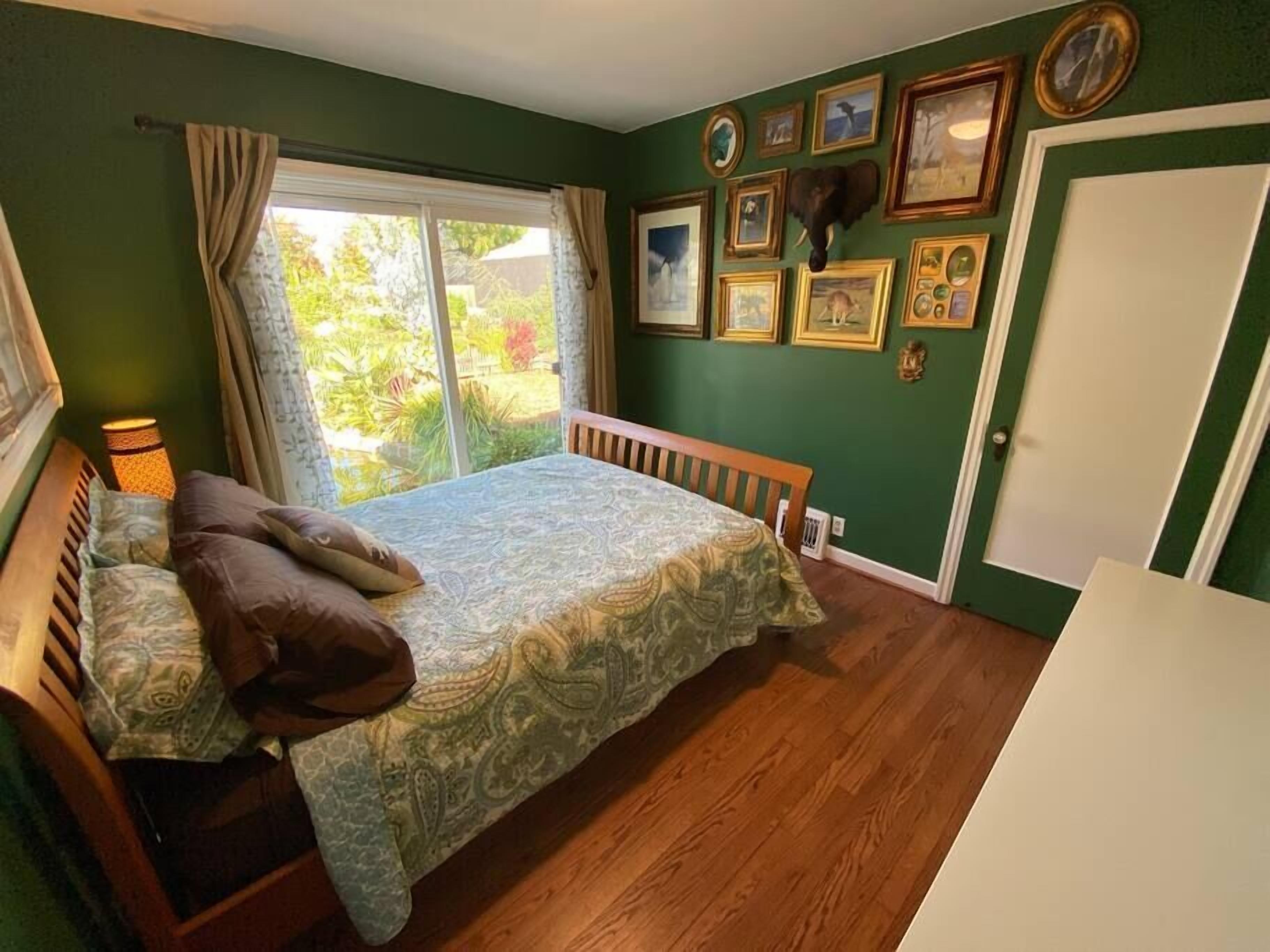 Une chambre à coucher avec un lit, une fenêtre avec des rideaux et un mur orné de tableaux.