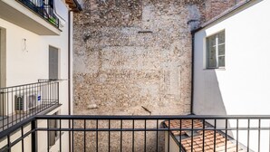 Ein Innenhof mit einer Steinmauer, einem Balkon mit Metallgeländer und einem Ziegeldach.