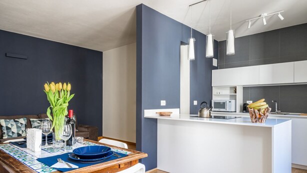 Eine moderne Küche mit einer zentralen Kochinsel, einem Essbereich mit Holztisch und einer Wand in dunkler Akzentfarbe.
