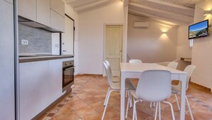 Une cuisine avec des meubles blancs, un sol carrelé et un coin repas comprenant une table et des chaises.