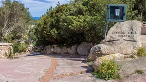 Un chemin de pierre mène à un panneau indiquant « PEVERO HILL CORPOD », d’où l’on peut admirer une zone boisée et, au loin, une étendue d’eau.