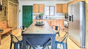 A kitchen with wooden cabinets, a stainless steel refrigerator, a dining table with chairs, and a green door. - Peaceful Nutrioso Cabin Retreat w/ Mountain Views! (Nutrioso)