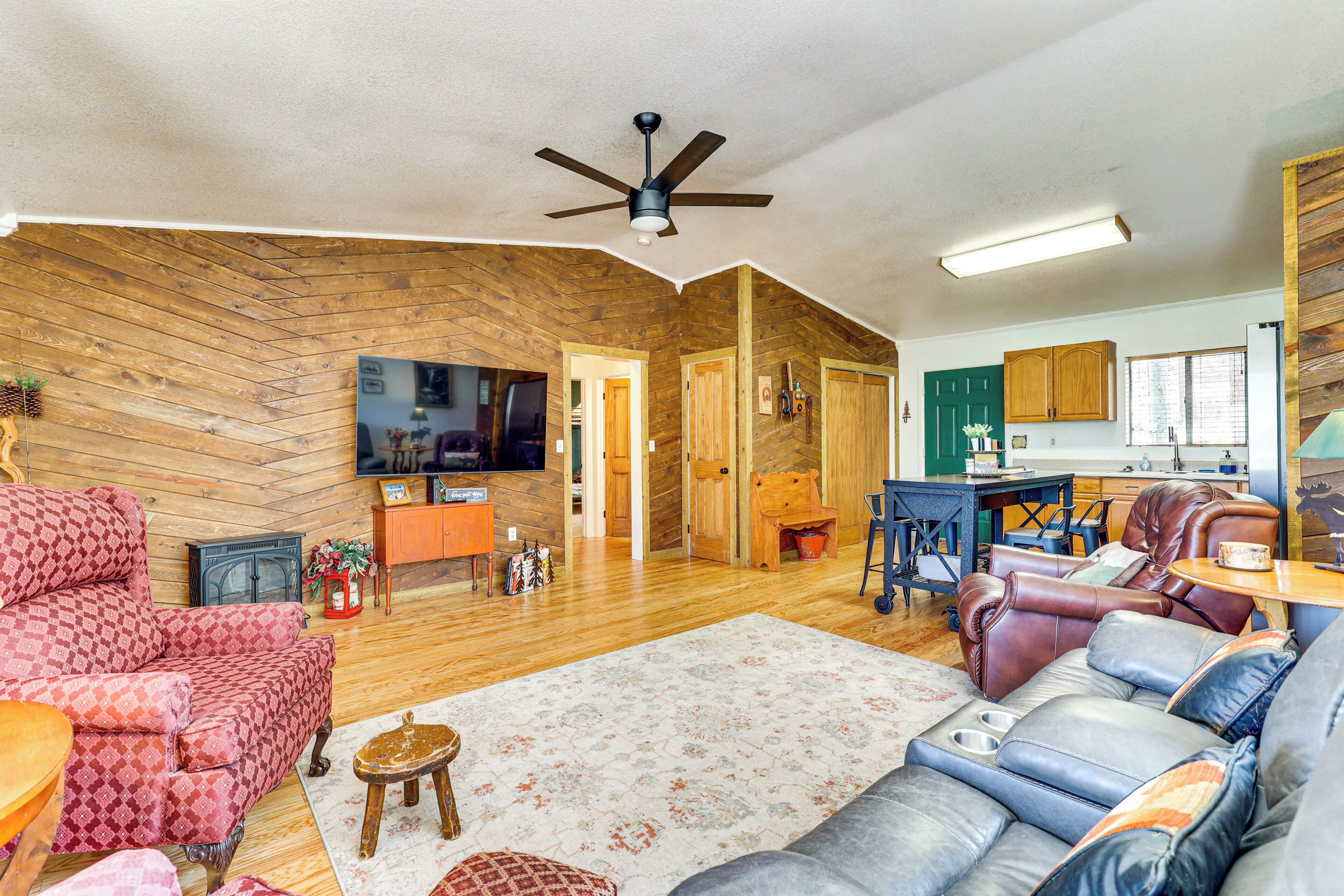 A spacious living room with a wooden herringbone floor, a ceiling fan, a flat-screen TV, a fireplace, and a dining area with a table and chairs.