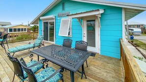 Una casa de playa turquesa con un patio, mobiliario exterior y una zona cubierta.
