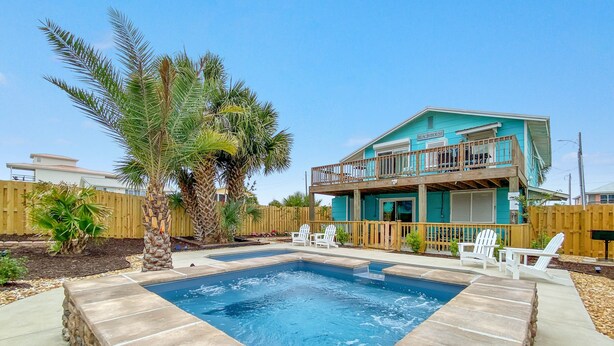 Una casa turquesa de dos pisos con balcón, piscina y sillas Adirondack blancas.