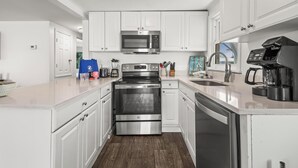Una cocina moderna con armarios blancos, electrodom ésticos de acero inoxidable y una cafetera.