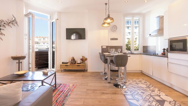 A modern kitchen with a dining area, a TV mounted on the wall, and a view of the city through the open door. - Downtown Cannes, walk to Beaches and Croisette (Cannes)