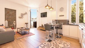 A modern living room with a sofa, coffee table, and a dining area with chairs and a table. There is a kitchen area with a sink and a window. - Downtown Cannes, walk to Beaches and Croisette (Cannes)
