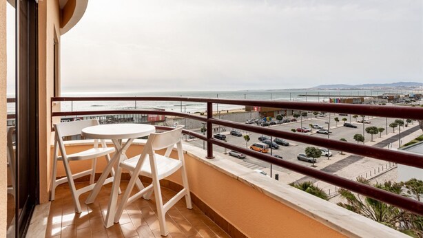 A balcony with a table and chairs, overlooking a beach and a parking area. - JOIVY Vibrant 2-bed flat w/ balcony (COSTA DE CAPARICA)